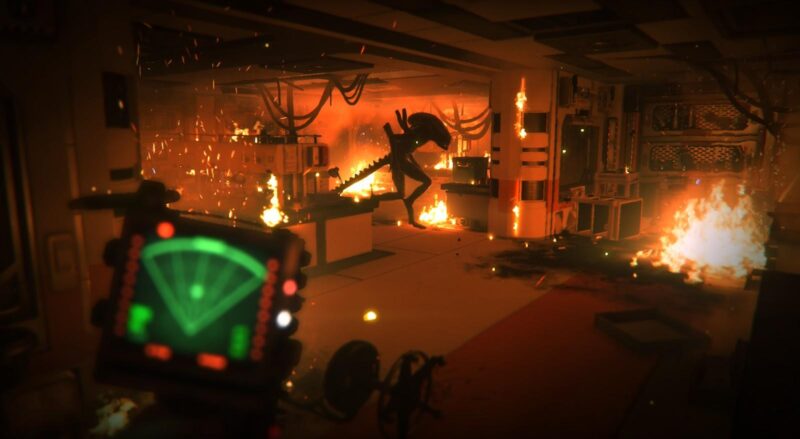 Imagem do jogo Alien: Isolation. Da esquerda para a direita, há um sensor de movimento com tela verde e preta fora de foco. No centro da imagem, mais ao fundo, há um Alien andando prestes a atacar cercado de um laboratório futurista em chamas. Há mesas, armários, cabos e líquidos desconhecidos espalhados para todos os lados.