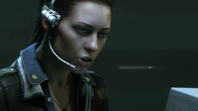 Imagem do jogo Alien: Isolation. É uma imagem em close up da personagem Amanda Ripley. A engenheira está com um semblante preocupado e utilizando um equipamento na cabeça que inclui um microfone e uma lanterna, presos À cabeça por uma tiara prateada. Ela olha e conversa atentamente em direção a um computador que está fora do quadro.