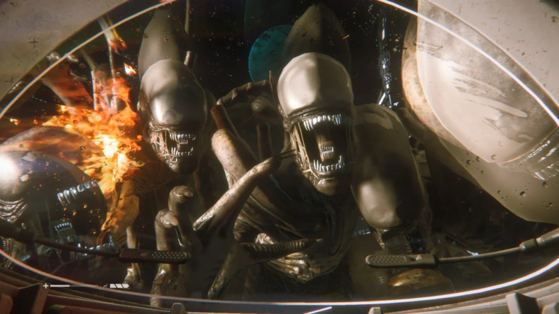 Imagem do jogo Alien: Isolation. Trata-se de uma cena na visão de Amanda Ripley. As bordas da imagem são curvas e tampadas e toda a imagem é repleta de reflexos de luz, pois Ripley está utilizando um capacete espacial. Na frente dela, quatro xenomorfos avançam em direção a ela. Todos estão com as bocas abertas, revelando uma segunda boca com os mesmos dentes brilhantes de dentro dela no lugar da língua. Em planos mais distantes, explosões e outros planetas no espaço são visíveis.