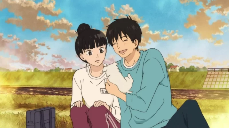 Cena do anime Que Chegue a Você: Kimi ni Todoke. Sawako, à esquerda da foto, tem o cabelo preto em um coque e está vestida com uma blusa branca de manga longa e uma calça da cor vinho. Ela tem os olhos bem abertos e uma feição surpresa. O Kazehaya de cabelo preto, à direita, usa uma blusa de manga longa da cor azul, calça preta e segura um filhote de cachorro da cor branca na direção da garota. Ele está sorrindo e com os olhos fechados. As duas personagens têm pele branca. Ao fundo, há uma paisagem rural, com poucas casas. O céu é um degradê de azul e tem algumas nuvens acinzentadas e douradas.