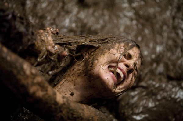 Cena do filme Arraste-Me para o Inferno Na imagem, a personagem Christine Brown está sendo atacada pelos braços de uma pessoa. Ela está com lama cobrindo todo o cabelo e sujando o rosto, em sua volta tem mais lama. Christine está com expressão de dor. Ela é uma mulher na faixa dos 30 anos, de pele clara e cabelos loiros. 
