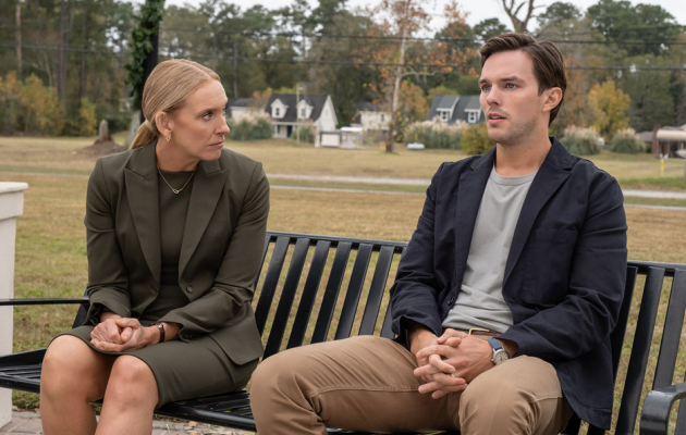 Na imagem estão Toni Collette e Nicholas Hoult. Ambos estão sentados em um banco preto. Nicholas está a direita, ele veste uma camisa cinza, uma calça bege e uma roupa preta por cima. Ela usa um terno e um vestido todo cinza escuro. Ela olha fixamente para Nicholas Hoult que não retribui o olhar.