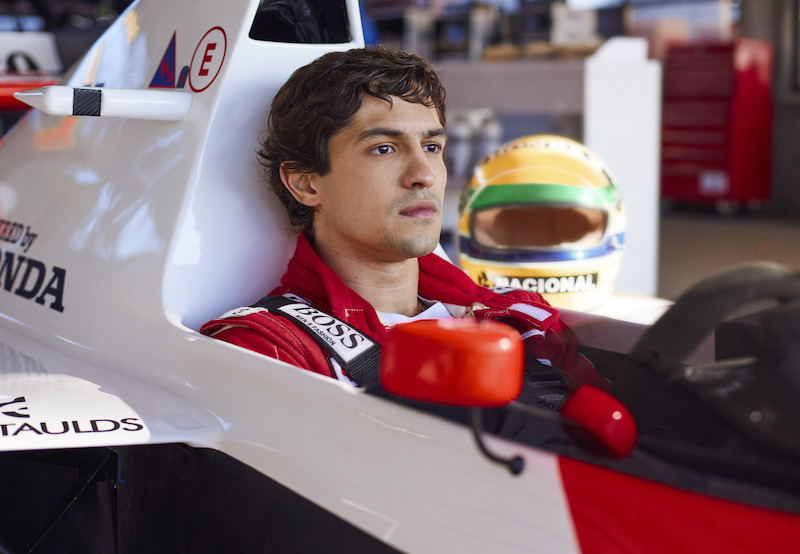 Cena de Gabriel Leone, com cabelos molhados de suor e sobrancelhas grossas, interpretando Ayrton Senna, dentro de sua McLaren, em concentração para a corrida que estava para acontecer. Seu capacete em segundo plano, marcado pelas cores de seu país, verde, amarelo e azul, iluminado pela luz clara do dia, dando uma aura de eterno e marcado por seus dois principais patrocínios, o Banco Nacional e a Honda.