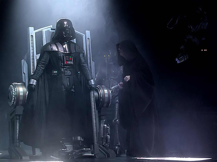 O cenário está quase todo escurecido. A única luz ilumina Darth Vader em uma maca, que agora está em pé. A luz vem de cima para baixo. Darth Vader está do lado esquerdo da imagem, e usa um traje preto e futurista. Ao seu lado, pouco visível, está Palpatine usando um capuz preto.