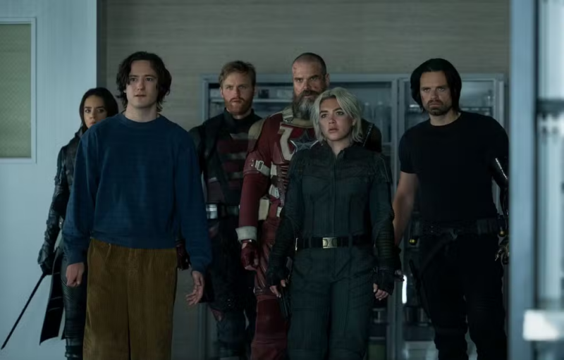 O cenário é de um laboratório. Seis personagens estão enquadrados. Na esquerda, ao fundo, está a Fantasma, na sua frente está Bob, com uma blusa azul e uma calça marrom. Mais ao fundo está o Agente Americano, uniformizado, sem capacete. Mais a direita está o Guardião Vermelho, também todo uniformizado e sem capacete. Mais a sua frente está Yelena, com suas roupas cinzas, e ao seu lado está o Soldado Invernal, com uma camisa preta e seu braço esquerdo mecânico aparente.