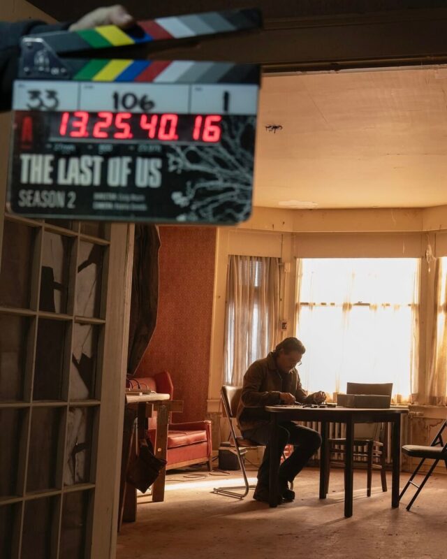 Ao lado esquerdo da imagem, existe uma claquete entreaberta com os números das tomadas que são gravadas no momento da foto e possui, na parte inferior do objeto, o nome do seriado, “The Last of Us” e “temporada 2”, escrito em inglês. Ao fundo, no lado direito da fotografia, Pedro Pascal, um homem chileno-americano com cabelos curtos, caracterizado de Joel, com um óculos no rosto, agasalhado com jaqueta de couro e cabelos grisalhos, interpreta o personagem da produção da MAX, que permanece sentado diante de uma mesa enquanto parece consertar algo com as mãos apoiadas sob a mesa. Atrás dele, há uma janela grande, iluminada por uma luz ensolarada.