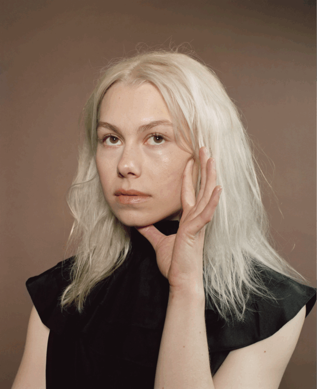 Ensaio de Phoebe Bridgers para a revista The Fader. Nela vemos Phoebe, uma mulher branca de cabelos platinados Ela veste um vestido preto de mangas curtas e está fotografada do busto para cima. Ela apoia a mão esquerda no queixo enquanto olha para cima. Ao fundo, uma parede na cor marrom claro