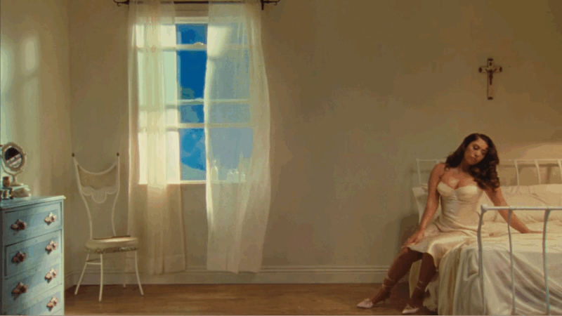 Kali Uchis está sentada à direita da imagem, sobre uma cama com lençóis brancos. Acima da cama, há uma cruz com a figura de Jesus. À esquerda da imagem, vê-se uma cômoda azul bebê com quatro gavetas; sobre ela, um espelho pequeno e redondo. Ao lado da cômoda, há uma cadeira branca posicionada próxima a uma janela com cortinas brancas. A cantora usa uma camisola branca de cetim, justa ao corpo.