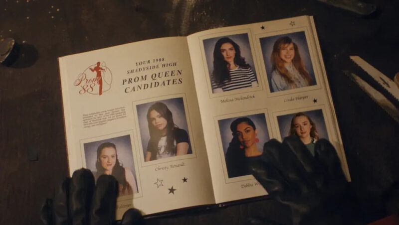 Na imagem, duas mãos vestindo luvas pretas folheiam um livro com imagens das candidatas para o título de rainha do baile. Há seis fotografias de garotas, duas na página à esquerda e quatro na direita. 