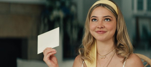 Cena do filme Eu Sei O Que Vocês Fizeram No Verão PassadoNa imagem, a personagem Danica segura um cartão de aniversário na mão direita. Ela olha para cima com uma expressão de riso. Danica é uma mulher branca, na faixa dos 25 anos, de cabelos loiros e usa uma faixa amarela na cabeça. 