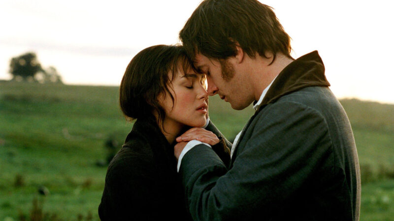 Cena do filme Orgulho e Preconceito (2005). Na imagem, os personagens Elizabeth Bennet e Mr. Darcy estão muito próximos, prestes a se beijar. Elizabeth, uma jovem branca de cabelos castanhos escuros presos, está com os olhos fechados, com as mãos tocando a mão de Darcy. Ela usa um casaco longo escuro. Darcy também tem a cabeça inclinada para frente e os olhos fechados, em um gesto de ternura. Ele veste um casaco escuro com gola alta. Ao fundo, há um campo verde sob um céu esbranquiçado ao entardecer, transmitindo um clima romântico e íntimo