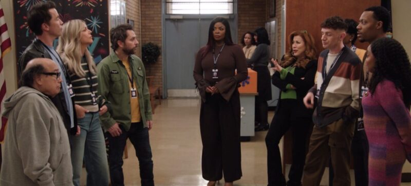 Na imagem, da esquerda para a direita, há um grupo de quatro pessoas, sendo um homem branco mais velho usando óculos e moletom cinza, um homem branco alto, com casco de couro e camiseta azul, uma mulher branca com cabelo loiro, blusa de manga longa listrada e calça jeans, e um homem branco de barba usando um casaco verde, uma camiseta amarela e uma calça jeans escura. Ao centro da imagem, há uma mulher negra de cabelo longo e liso, usando um suéter marrom e calças pretas. Ao lado direito, há um um outro grupo de quatro pessoas, sendo uma mulher branca de cabelo longo e ruivo, usando um suéter preto, blusa verde e calça preta, um homem branco de cabelo cacheado e suéter listrado colorido, um homem negro de cabelo curto e uma mulher negra de cabelo longo e cacheado usando um vestido listado e colorido. 