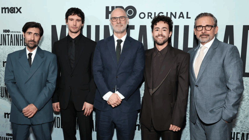 Durante a premiére do filme, cinco homens posam juntos em frente a um painel da HBO. Eles vestem ternos em tons variados de azul, preto e cinza. Estão lado a lado, sorrindo levemente para a câmera, em clima formal de evento de estreia.