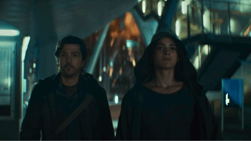 Em primeiro plano há dois personagens: Cassian Andor à esquerda e Bix Caleen à direita. Cassian é um homem de pele clara mais velho com barba e cabelos pretos. Está com o olhar determinado e usa um casaco preto por cima de uma camiseta escura. Bix é uma mulher parda de cabelo enrolado e preto. Ela está com o mesmo olhar determinado que o namorado e utiliza um capuz cinza. Atrás de ambos está, fora de foco, um prédio Coruscant, uma cidade de aspecto futurista, e um prédio atrás dele está em chamas por causa de uma explosão.
