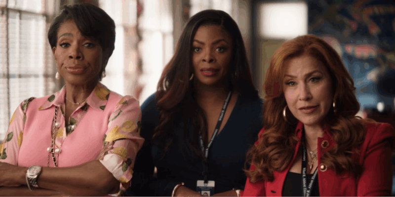 Na imagem, da esquerda para a direita, há uma mulher negra de cabelo liso e curto, usando uma blusa rosa e com estampas floridas, um colar de pérolas e um relógio no pulso. Ao centro, há uma mulher negra de cabelo liso e longo, usando um vestido azul marinho e um crachá no pescoço. Ao seu lado, há uma mulher branca de cabelo longo e ruivo, usando brincos dourados, uma blusa vermelha e um crachá no pescoço. 