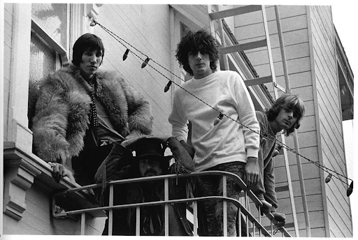  Fotografia em preto e branco mostrando os integrantes do Pink Floyd na sacada de um prédio. Da direita para a esquerda: Nick Mason apoiado na grade, Roger Waters usando um casaco de pele, Syd Barrett em destaque com blusa branca e cabelo desgrenhado, e Richard Wright inclinado para frente, segurando a barra do corrimão. Entre eles há luzes decorativas penduradas e, ao fundo, parte de uma escada lateral externa