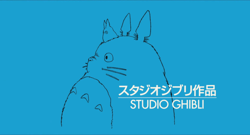 Esta é uma imagem com o logo do Studio Ghibli, um famoso estúdio de animação japonês. O fundo é de um azul vibrante e sólido. No centro, há um desenho de contorno preto do personagem Totoro, uma criatura grande e peluda com orelhas pontudas, visto de perfil. Em cima de sua cabeça, há um Totoro menor. Sobre a imagem, está escrito "STUDIO GHIBLI" em letras brancas, com caracteres em japonês logo acima.