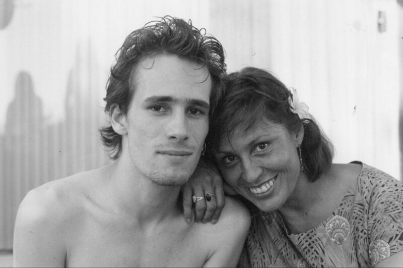 Cena do filme It’s Never Over, Jeff BuckleyNa imagem, em preto e branco, está o cantor Jeff Buckley com sua mãe Mary Guibert. Ele, no canto esquerdo, está com o rosto próximo de sua mãe, braços abaixados e sorriso forçado, posando para a foto. Seus cabelos lisos estão penteados para cima e parecem molhados. Ele está sem camisa. O cantor possui pele clara e barba por fazer. Já Mary está com uma das mãos apoiada no ombro do filho e repousa a cabeça em cima. Ela está com um sorriso largo e usa uma flor presa no cabelo, acima da orelha esquerda. Nos dedos, usa um anel. Ela veste uma roupa estampada, possui pele clara e cabelos na altura do pescoço.