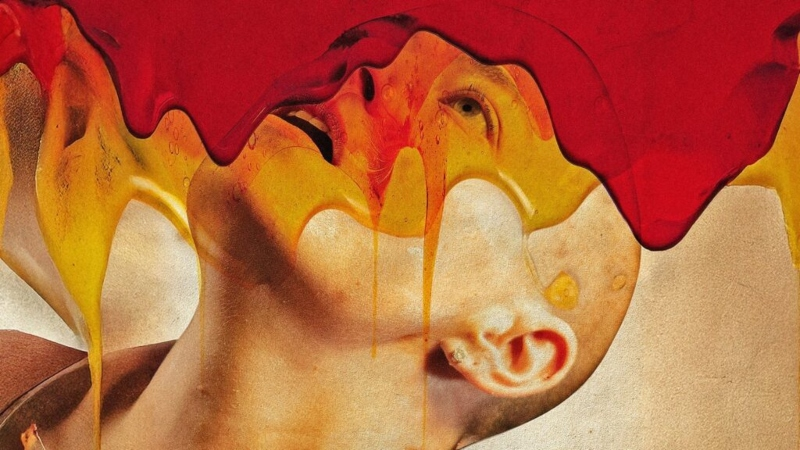 Imagem de Bugonia, filme de Yorgos Lanthimos. Na foto vemos a personagem Michelle, uma mulher branca com a cabeça raspada, olhando para cima. Na região de cima da imagem escorrem dois líquidos sobrepostos, um na cor vermelha e outro na cor amarela.