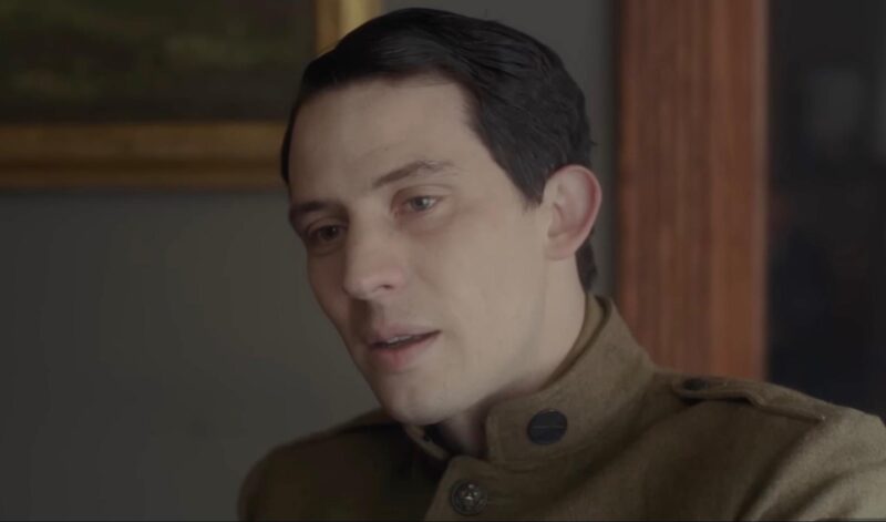 David, um homem branco, de cabelos castanhos e olhos claros, aparece com um uniforme militar e cabelo penteado com gel. Seus olhos parecem tristes e marejados de lágrimas. 