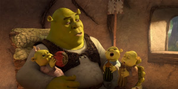 Fotografia de Shrek, ogro verde com uma camisa bege e colete marrom, segurando seus três filhos no colo enquanto os amamenta com mamadeiras feitas de chuchu. Os bebês são semelhantes ao pai fisicamente porém, pequenos. Eles vestem roupas rosa, azul e bege, respectivamente da esquerda para a direita, enquanto arrotam. 