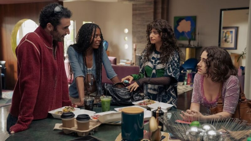 Cena da série I Love LA. A imagem apresenta um grupo de amigos na sala de estar: da esquerda para direita, há um homem branco com barba e cabelos castanhos cacheados que veste uma blusa vermelha, uma mulher negra com tranças que usa uma camiseta azul entreaberta, uma mulher branca de cabelos encaracolados que utiliza um moletom verde com azul e branco, e uma mulher branca de cabelos ondulados que veste uma blusa rosa e roxa. Eles estão se encarando e estão na frente de uma mesa com utensílios e comidas. 