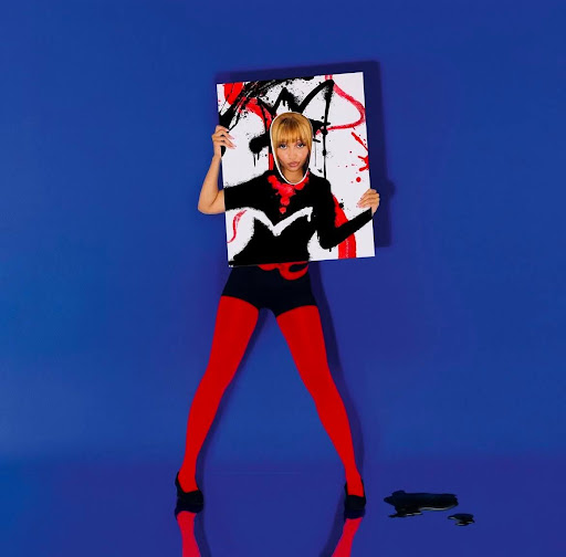  A imagem é a capa do álbum Fancy Some More, de PinkPantheress. Nela, a cantora aparece em frente a um fundo azul vibrante, vestindo meia-calça vermelha, sapatos pretos e um body preto com detalhes vermelhos. Ela segura um quadro pintado com traços expressivos em preto e vermelho, com um recorte central que revela seu rosto, criando a ilusão de que a pintura se prolonga em seu corpo. No chão, uma pequena mancha de tinta preta reflete parte da cena. A composição mistura arte e moda de maneira ousada, traduzindo o estilo visual experimental e criativo da artista.