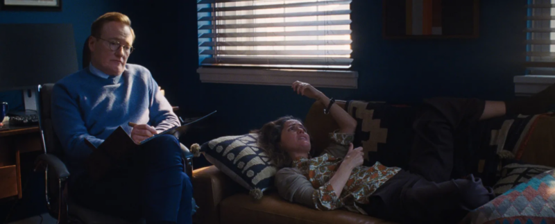 Linda está em na sala de consultório azul de seu terapeuta, que está sentado à esquerda cum uma expressão indiferente, enquanto ela está deitada no sofá à direita com a mão na cabeça e uma expressão triste no rosto.