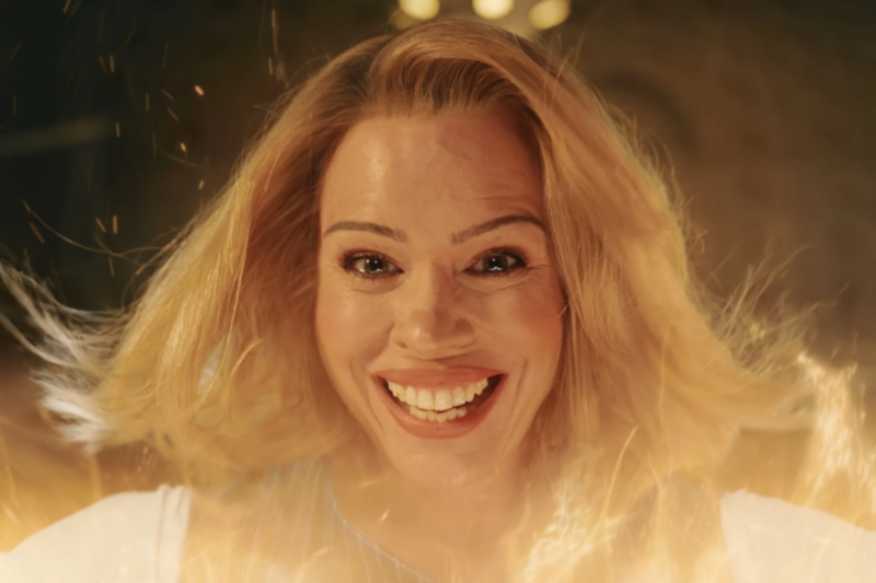 Na imagem, Rose Tyler sorri diretamente para a tela enquanto feixes de luz dourados do processo de "regeneração" cercam todo o corpo dela. Rose é uma mulher branca de cabelos loiros e olhos castanhos.
