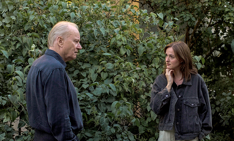 Cena do filme Valor Sentimental. Na imagem, há um homem branco de cabelos louros grisalhos olhando para uma mulher branca de cabelos castanhos. Eles estão em frente a diversos arbustos. Ele veste uma camisa social e ela usa uma blusa preta com uma jaqueta jeans por cima.