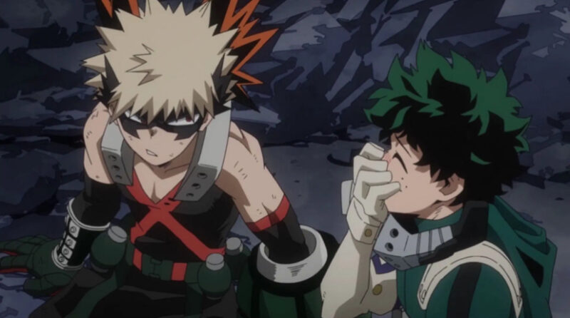 A imagem mostra um frame do anime. À esquerda, vemos um menino loiro de pele branca usando uma máscara preta com detalhes laranjas nas pontas afiadas que chegam até suas orelhas. Ele usa um uniforme preto com um marcas laranjas e ombros cinzas, luvas com as mesmas cores e calça preta, ao redor de sua cintura está um cinto com pequenas bombas. Ele olha com uma expressão agressiva para o personagem ao seu lado. À direita, está um menino de pele branca, cabelo verde bagunçado e olhos da mesma cor, vestindo um uniforme verde com detalhes brancos, luvas brancas, um capuz verde e uma máscara cinza. Ele está com uma das mãos sobre a boca, rindo. Ao fundo, vemos chão e paredes de pedra.