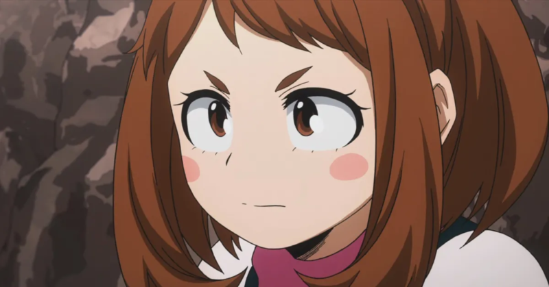A imagem mostra um frame do anime. Uma menina aparece ao centro, com pele branca, cabelos curtos castanhos e olhos da mesma cor. Ela está próxima da câmera, suas bochechas são rosadas e ela olha para o lado esquerdo, com uma expressão determinada. Podemos ver a gola cor de rosa de sua roupa, com ombros em um rosa mais claro. Ao fundo, é possível ver uma parede de pedras.