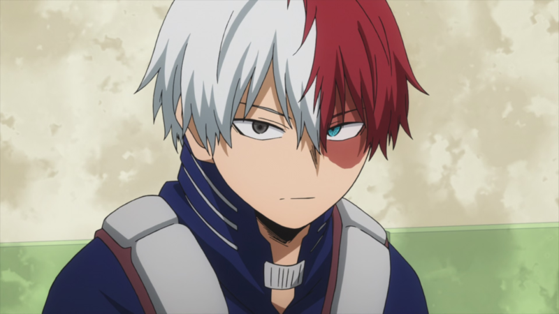 A imagem mostra um frame do anime. Um menino aparece ao centro, com pele branca e cabelo repartido ao meio. Ao lado esquerdo, seu cabelo é da cor branca, com um olho castanho, ao lado direito, o cabelo é vermelho, com um olho azul. Ao redor do olho azul, ele possui uma cicatriz vermelha que vai até o topo de seu rosto. Ele usa um uniforme azul com detalhes cinzas. Está com uma expressão séria. Ao fundo, vemos uma parede bege com o rodapé verde claro.