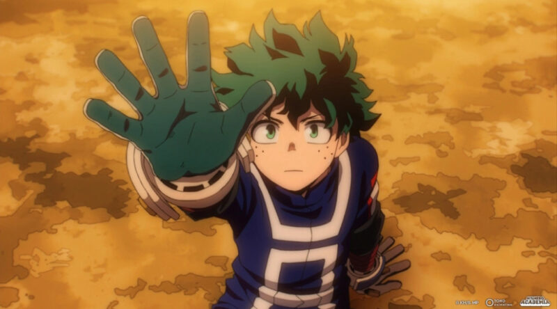  A imagem mostra um frame do anime. Um menino aparece ao centro, com pele branca, cabelo verde bagunçado e olhos da mesma cor, vestindo um uniforme azul com detalhes brancas e luvas verdes. Ele está sentado no chão, apoiado em uma das mãos, enquanto a outra está erguida, como se precisasse alcançar algo. A expressão no rosto dele é séria e determinada. Ao fundo, vemos um terreno alaranjado e desgastado.