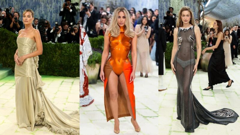 Montagem com três celebridades posando no tapete do Met Gala diante de fotógrafos e convidados. À esquerda, uma mulher usa um vestido tom champagne tomara que caia, com tecido drapeado e longa cauda acetinada. No centro, outra mulher veste um look futurista laranja brilhante, semelhante a uma armadura metálica, combinado com uma saia de fenda frontal. À direita, uma modelo usa um vestido preto transparente e brilhante, justo ao corpo, com detalhes prateados e cauda longa. O ambiente é iluminado com diversos fotógrafos ao fundo registrando os looks.