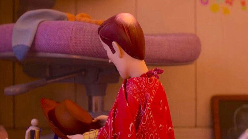 Cena do filme Toy Story 5 Na imagem da animação, o personagem Woody está de costas, revelando a ausência de tinta no topo da cabeça, como se fosse uma calvície. Ele está vestindo um poncho vermelho, amarrado no pescoço, com algumas figuras em branco. Woody está apoiando seu chapéu de caubói em alguma superfície. Ele possui a aparência de um caubói, de pele clara e cabelos curtos e lisos na cor castanha.