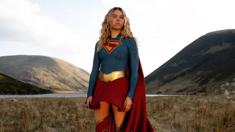 Cena do Filme. Kara, uma jovem mulher vestida com o uniforme de Supergirl, que é azul de manga longa com o símbolo vermelho e amarelo com 
