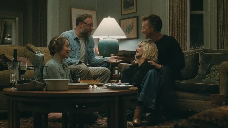 Cena de O Convite. Os quatro personagens estão reunidos na sala do apartamento. À esquerda, Joe, interpretado por Seth Rogen, e Angela, vivida por Olivia Wilde, sorriem enquanto conversam com Hawk, interpretado por Edward Norton, e Pína, vivida por Penélope Cruz, sentados à direita. Entre eles há uma mesa de centro com taças, garrafas, pratos e outros utensílios. Ao fundo, um abajur aceso ilumina a sala, decorada com quadros, sofás, poltronas e cortinas em tons neutros.