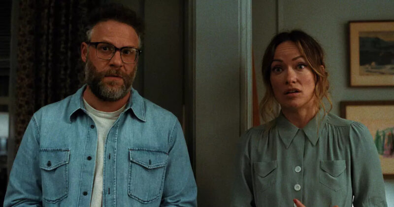 Cena de O Convite. Joe, interpretado por Seth Rogen, e Angela, vivida por Olivia Wilde, aparecem lado a lado, separados por uma parede atrás deles. Joe usa uma camisa jeans clara sobre uma camiseta branca e óculos de armação escura, enquanto Angela veste uma camisa verde-clara de mangas longas. Os dois olham para a frente com expressões de surpresa. Ao fundo, há uma parede em tom verde com quadros decorativos.