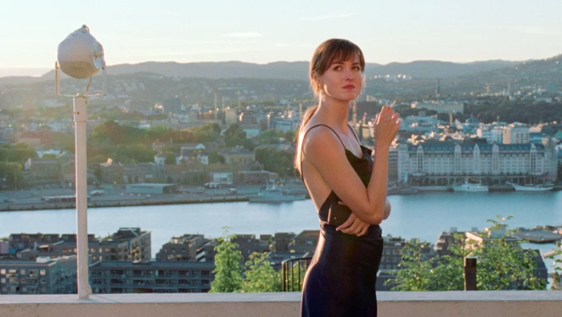 Cena de A Pior Pessoa do Mundo. Na imagem, há uma mulher branca de cabelos castanhos olhando para cima. Ela está na sacada de um edifício. Atrás dela, há a paisagem de Oslo, cidade da Noruega.