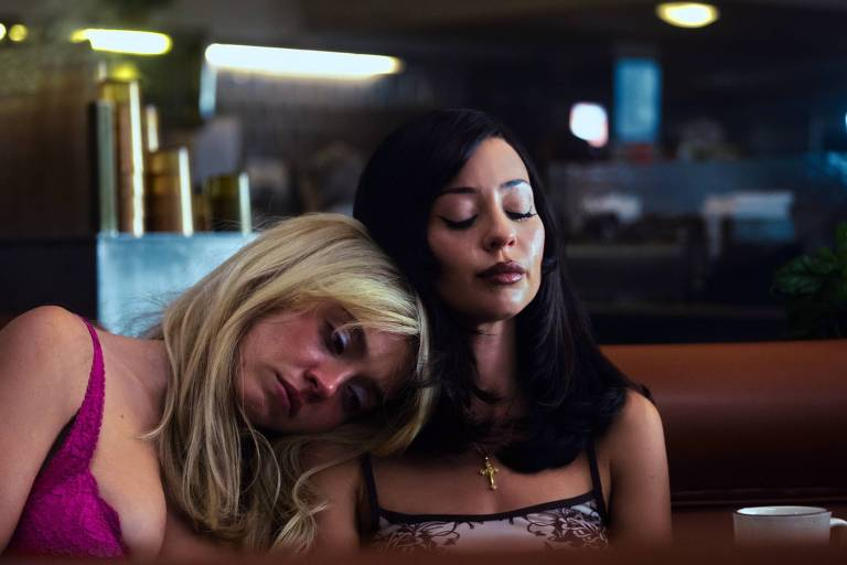 Cena da 3° temporada de Euphoria. Plano fechado de Cassie (Sydney Sweeney) e Maddy (Alexa Demie) lado a lado num restaurante com iluminação acolhedora e intimista. À esquerda, Cassie, mulher branca, loira, com maquilhagem nos olhos e um top de renda cor-de-rosa vivo, repousa a cabeça de forma exausta no ombro de Maddy, olhando para baixo. À direita, Maddy, mulher latina de cabelos pretos longos e lisos e top com padrão floral castanho e branco, surge de olhos fechados com uma expressão compenetrada, usando um crucifixo dourado no peito. 