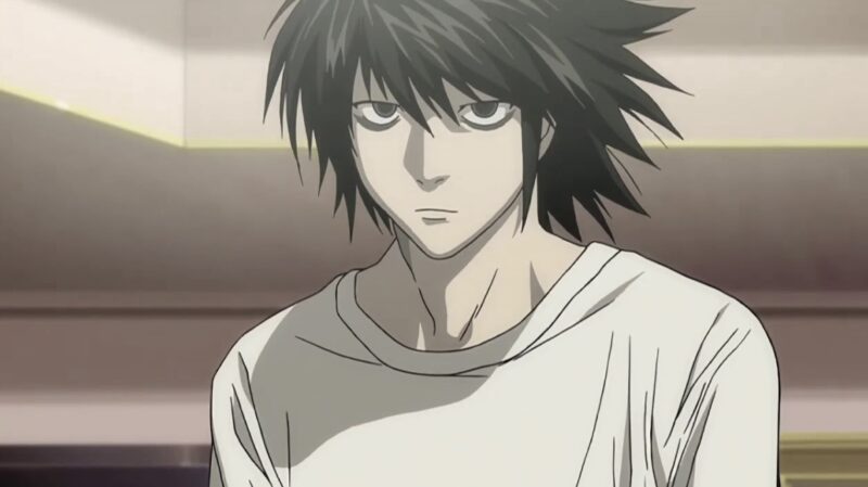 Cena do anime Death Note. A imagem centraliza um homem pálido, com cabelos pretos e longos, usando uma camiseta branca. Ele possui uma expressão séria e possui olheiras escuras abaixo de seus olhos, parece cansado. Ao fundo, vemos paredes da cor bege.
