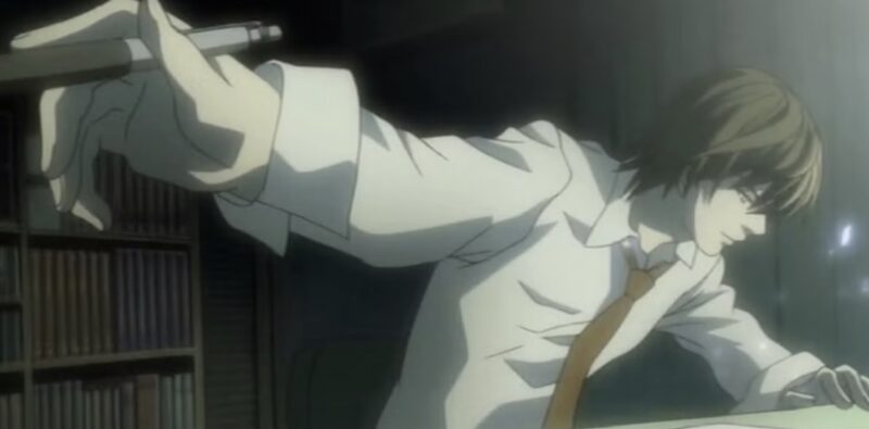 Cena do anime Death Note. Vemos um homem segurando uma caneta. Ao lado esquerdo, sua mão está levantada, onde podemos ver a caneta. Ao lado esquerdo, vemos seu rosto. O homem é branco, com cabelos e olhos castanhos e usa uma camisa branca com gola, além de uma gravata marrom. Ele olha para baixo com uma expressão séria, onde podemos ver uma mesa e um papel. Ao fundo, vemos uma estante cheia de livros e um quarto escuro.
